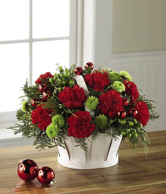  Rich red roses and red carnations are accented with green hypericum berries, green button poms, clusters of shining red glass holiday balls, and an assortment of fragrant Christmas greens. Arranged to perfection in a white wash woodchip basket, standard size