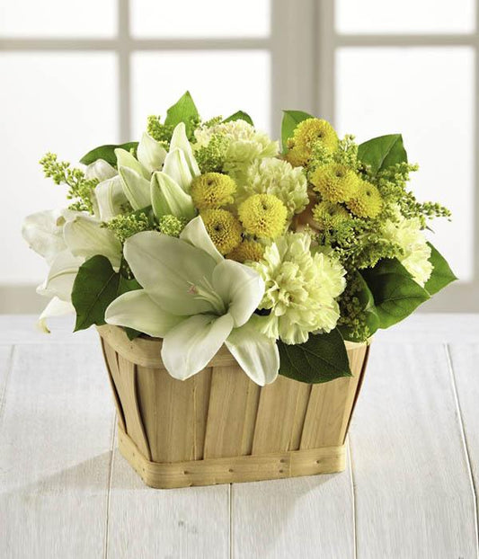 Yellow roses, carnations, button poms, and solidago shed light on any situation mingling with white Asiatic Lilies and lush greens arranged beautifully in a rectangular woodchip basket. standard size