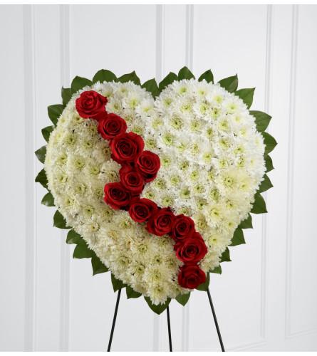 Pearly white chrysanthemums form the shape of a heart, accented with greens lined around the outside and "broken" in the middle with a line of rich red roses to create an exquisite way to honor the life of the deceased at their memorial service. Displayed on a wire easel.