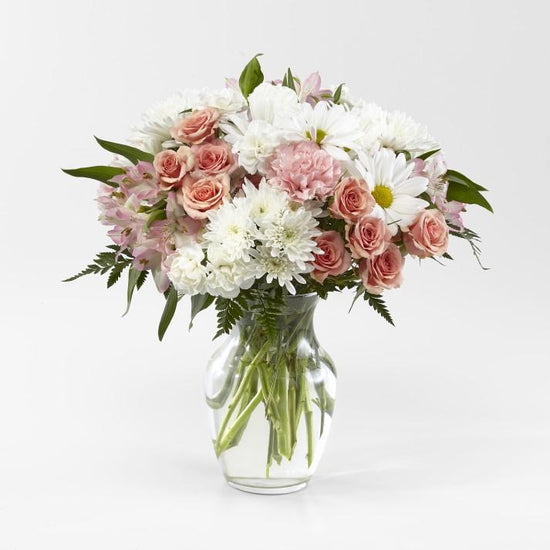 pink and white blooms of spray roses, alstroemerias, white daisy pom poms, carnations and lush greens in a clear glass vase
