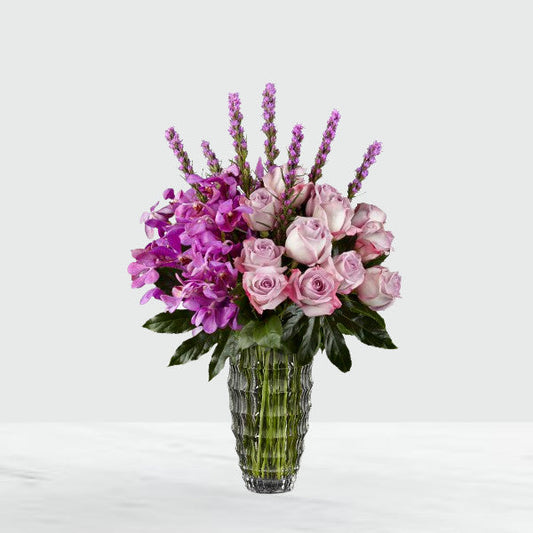 Notice the lavender swirl of roses offset by the fanciful layers of petals brought on by stems of lavender Mokara Orchids with a crown of purple liatris extending from the top. Arranged to perfection in a clear faceted glass vase