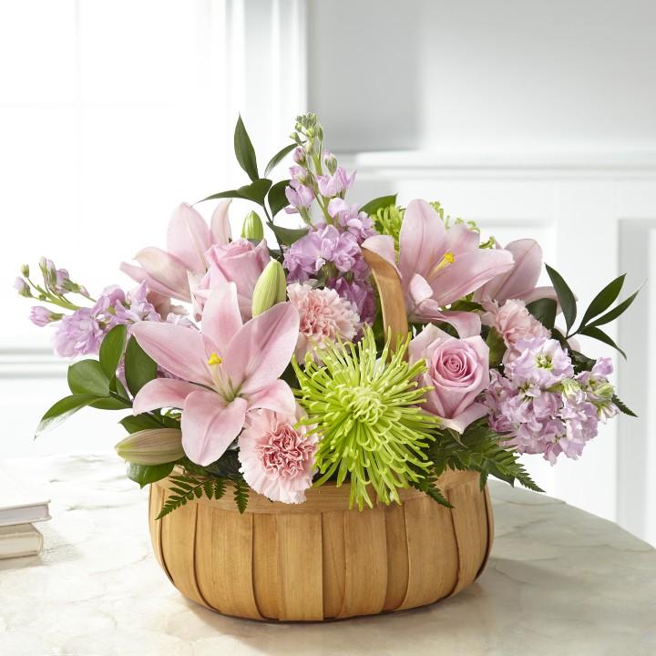 pink lilies, pink canrations, pink roses, lavender stock, and green spider mums with lush greens in a basket