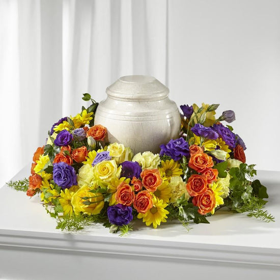 tabletop ring of flowers is handcrafted by a local florist includes blooms of orange spray roses, purple lisianthus, yellow daisy pom poms, and light yellow carnations