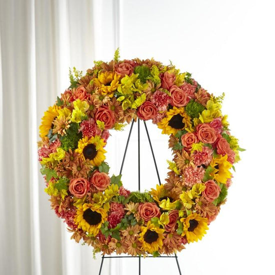 The vibrant shades of fall are curated with a collection of sunflowers, dianthus and roses in our Autumnal Memories Wreath. 