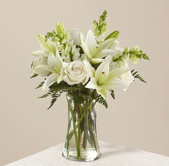all white blooms of lilies, roses, and snapdragons in a clear glass vase