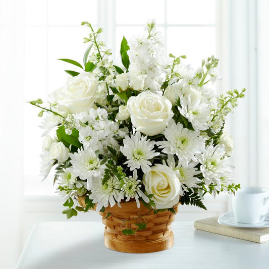  white roses, stock, cushion pompons and larkspur set among complementary greens in a basket. standard size